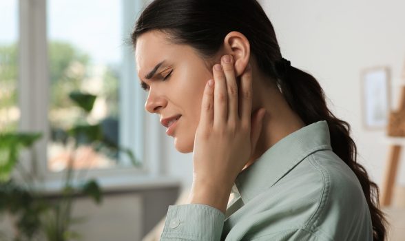 Young woman suffering from ear pain in room